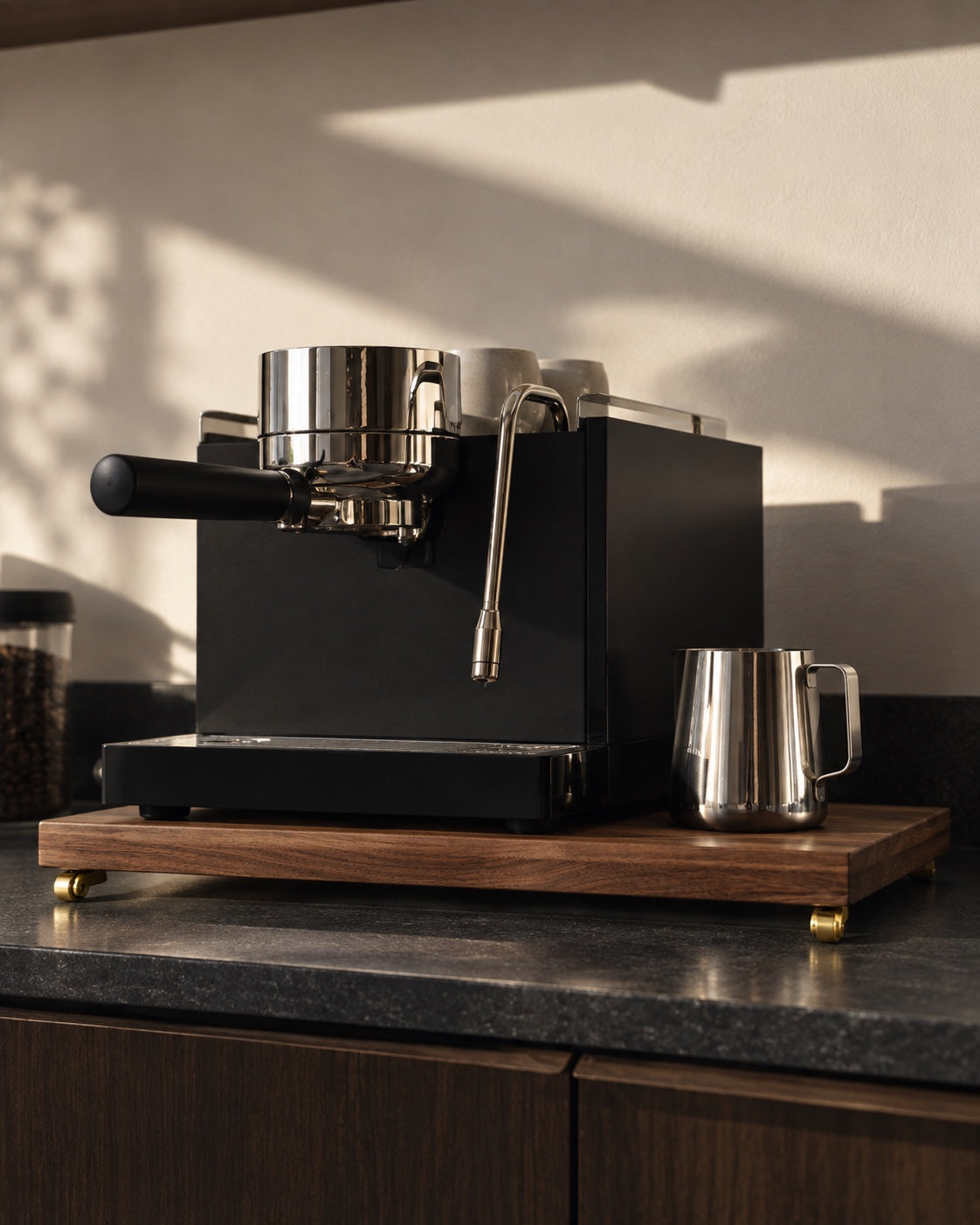 Black espresso machine on The Press walnut platform with brass casters in warm natural light